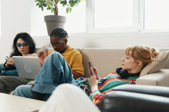 young adult colleagues socializing and working in a modern workplace, diverse coworkers collaborating and using digital devices, Gen Z friends sharing ideas comfortably