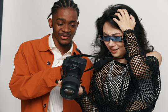 Young adult man and woman colleagues examining camera photos while socializing at workplace, showing business teamwork and Gen Z coworkers interaction with excitement.