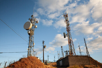 Torres de telecomunicação no topo de uma montanha com vegetação seca, capturadas durante o pôr do sol. O contraste entre natureza e tecnologia com a paisagem urbana ao fundo. © valmir