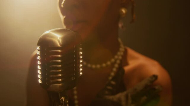 Close up shot of unrecognizable Black woman singing to retro microphone while performing on stage in golden lighting with lens flare, copy space