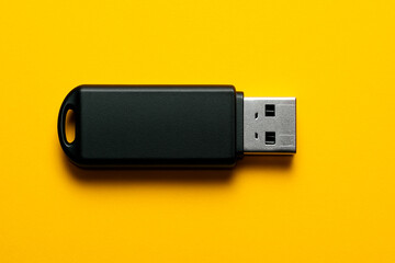 A sleek black USB flash drive lies horizontally on a vibrant yellow background, offering a minimalist and versatile shot for technology, data, and storage concepts.