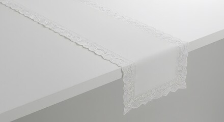 A white lace runner elegantly placed atop a clean, white table surface, creating a minimalist aesthetic.