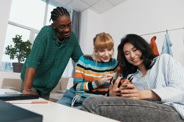 Young adult woman coworkers socializing at workplace, smiling friends using smartphone, business...