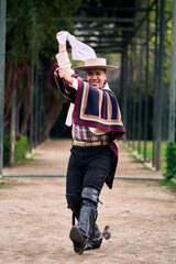 Portrait of a smiling, cheerful young man dressed as a Chilean huaso, celebrating and posing to...