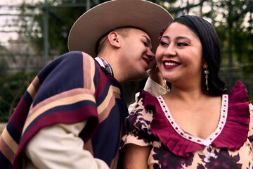 Portrait of a smiling young couple, dressed as Chilean huasos, posing romantically, about to kiss...