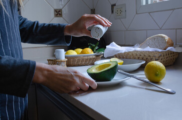 Woman's hands preparing avocado with lemon and salt in the kitchen.