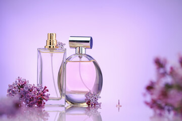 Bottles of perfume and lilac flowers on mirror surface against violet gradient background,...