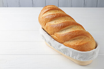 One bread loaf in basket on white wooden table, space for text
