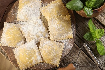 Uncooked ravioli and basil on wooden table, top view