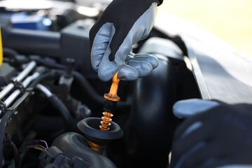 Worker checking motor oil level in car with dipstick, closeup