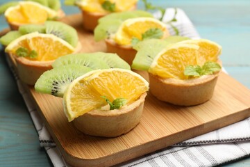 Tartlets with fruits and mint on light blue wooden table, closeup. Delicious dessert