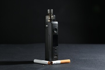 Electronic smoking device and broken cigarette on dark table against black background, closeup