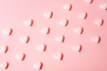 White heart shaped candies on pastel pink background with bright light and shadows. Valentines day concept. Top view