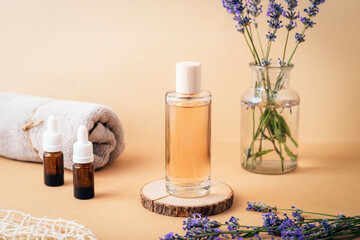 Glass cosmetic bottle with perfume, essential oils, towel and fresh lavender flowers on beige...