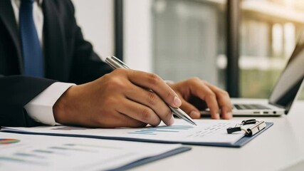Close up of businessman analyzing financial charts and working on laptop in office - Powered by Adobe