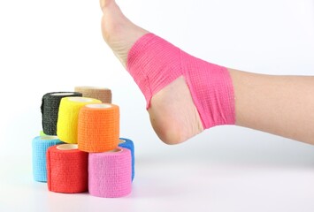 Woman foot with a pink cohesive bandage wrapped in the ankle isolated in a white background