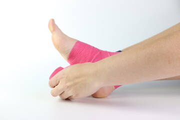 Woman foot with a pink cohesive bandage wrapped in the ankle isolated in a white background