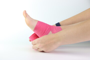 Woman foot with a pink cohesive bandage wrapped in the ankle isolated in a white background