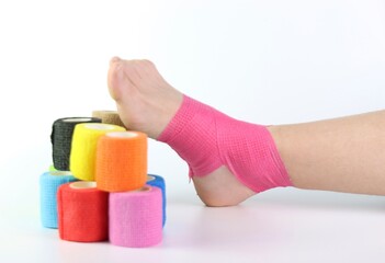 Woman foot with a pink cohesive bandage wrapped in the ankle isolated in a white background