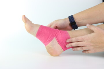 Woman foot with a pink cohesive bandage wrapped in the ankle isolated in a white background