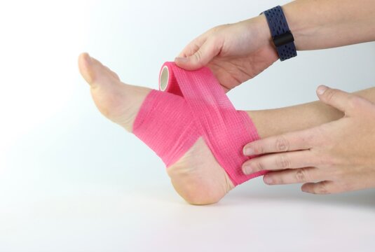 Woman foot with a pink cohesive bandage wrapped in the ankle isolated in a white background