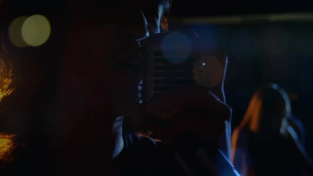 Male singer gripping vintage microphone and singing to energize crowd while animated bokeh drifting