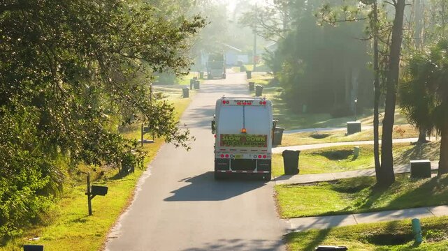 Garbage truck collecting curbside trash bins in American neighborhood, part of regular waste management in clean and organized suburban area.