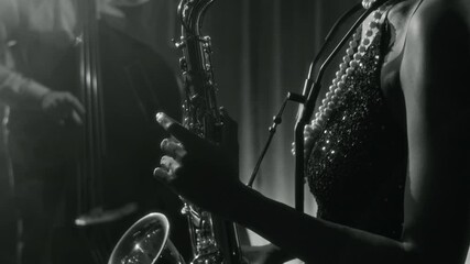 Close up black and white shot of glamorous Black woman playing saxophone during jazz performance on stage in vintage club, side view