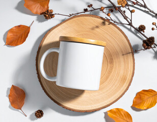 Coffee mug on wooden tray surrounded by green leaves, wood slices and pinecones on white background