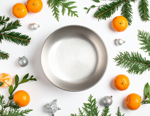 Stainless bowl surrounded by whole and sliced tangerines with green leaves on a clean white surface