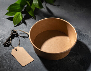 Clay bowl with blank tag and antique key surrounded by green leaves on dark textured surface