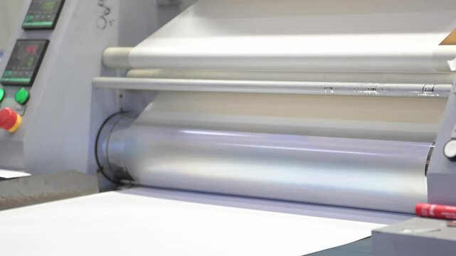 An industrial laminator with rotating shafts laminates, applies a transparent film to paper in the production room of the printing house