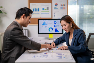 Two people are sitting at a desk with a computer monitor in front of them