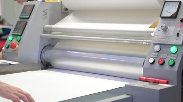 An industrial laminator with rotating shafts laminates, applies a transparent film to paper in the production room of the printing house