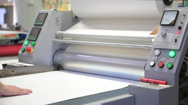 An industrial laminator with rotating shafts laminates, applies a transparent film to paper in the production room of the printing house