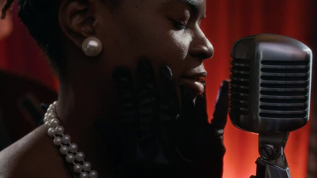 Close up of glamorous Black woman singing to microphone on stage with focus on mouth and retro mic