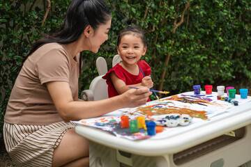 happy mother and toddler girl painting watercolor in paper at backyard.