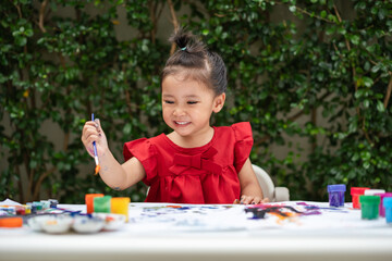 happy toddler girl painting watercolor in paper at backyard.