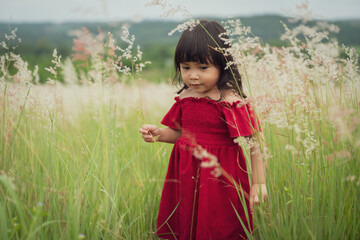 toddler girl in red dress playing grass flower in field
