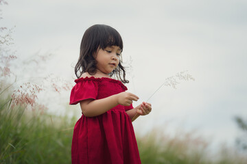 toddler girl in red dress playing grass flower in field