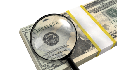 Magnifying glass inspecting a stack of twenty us dollar bills on a transparent background.