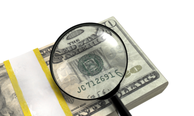 Magnifying glass inspecting the back of a stack of us dollar bills on a transparent background.
