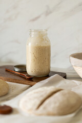 Freshly prepared sourdough bread dough rests on parchment near a container of active starter and a...