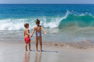 Happy kids have fun in sea surf on white sand beach. Couple of children sit in water pool. Travel lifestyle, swimming activities in family summer camp. Vacations on tropical island.