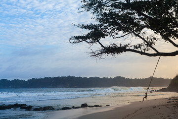 Happy girl have fun swinging high in mid air. Flying on rope swing on sea beach. Travel adventure...
