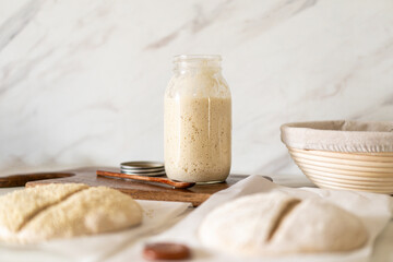 Freshly prepared sourdough bread dough rests on parchment near a container of active starter and a...
