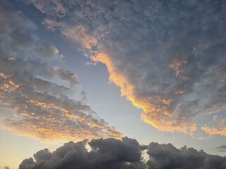 Fototapeta premium Dark thick clouds with soft upper layer lit by sunrise, contrasting textures of morning sky showing golden light above stormy cloudscape.