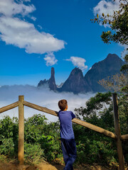 Boy on his back looking at the mountain peaks emerging from the cloud cover