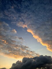 Dark thick clouds with soft upper layer lit by sunrise, contrasting textures of morning sky showing golden light above stormy cloudscape.