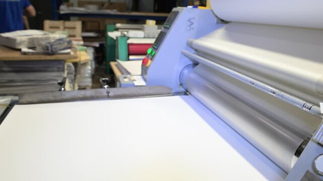 An industrial laminator works by laminating, applying a transparent film to paper in the production room of a printing house